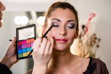 Makyaj sanatçısı, genç ve güzel bir bayana profesyonel makyaj yapıyor.