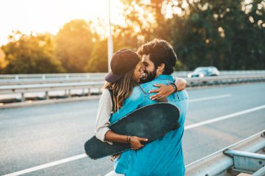 Genç çift şehir caddesinde paten kayarken eğleniyor. Sokakta durup sarılıyorlar..