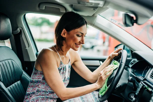 Interior car detailing. Happy middle age woman wipes and cleans the interior of her car.