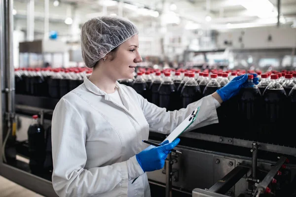 Jonge Vrolijke Vrouwelijke Werknemer Bottelfabriek Controleert Sapflessen Voor Verzending Inspectiekwaliteitscontrole — Stockfoto