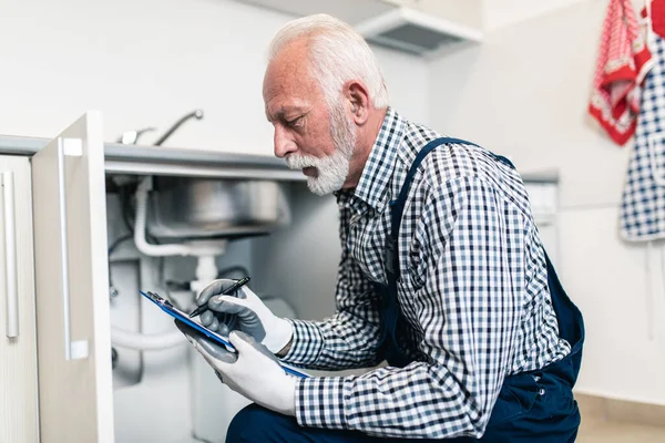 Senior man plumber working with plumbing tools on the kitchen. Renovation.