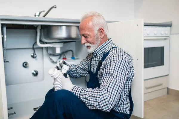 Senior man plumber working with plumbing tools on the kitchen. Renovation.