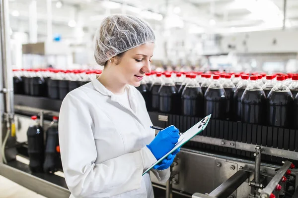 Jonge Vrolijke Vrouwelijke Werknemer Bottelfabriek Controleert Sapflessen Voor Verzending Inspectiekwaliteitscontrole — Stockfoto