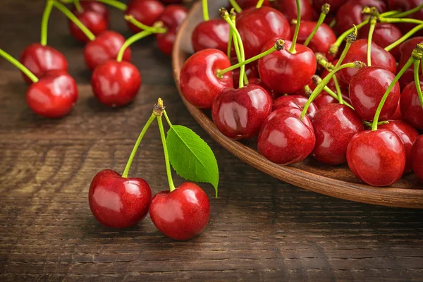 Two ripe cherries on the background of a village table, a bunch of cherries in a clay dish and scattered on a tabl.