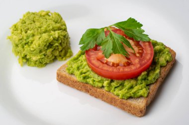 Bir dilim domates ve doğranmış avokado hamuru beyaz bir plaka üzerinde avokado tost.