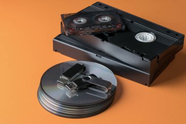 Kompakt diskler ve video-ses kasetleri ve turuncu bir arka plan üzerinde bir flash sürücü yığını.