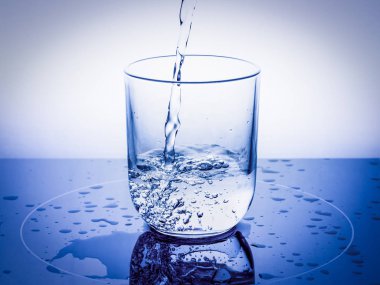 Bir jet su kabarcıkları ile bir bardak içine dökülen ve mavi bir arka plan üzerinde damla.