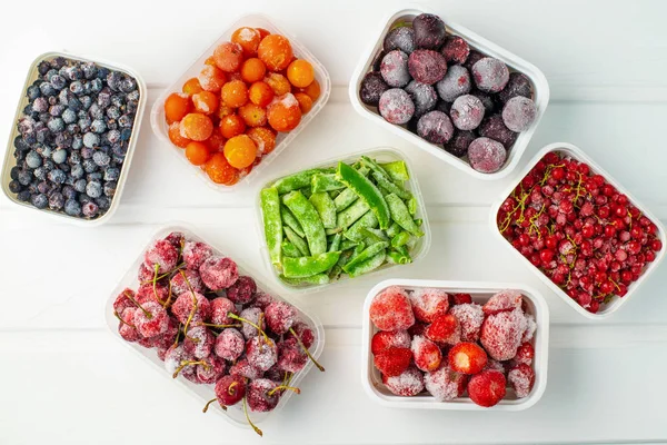 Заморожені ягоди та овочі в пластикових коробках на білому дерев'яному фоні — стокове фото