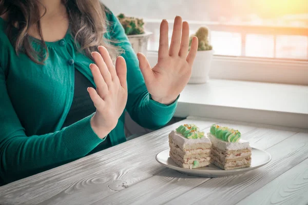 Jovem sentada à mesa com gestos de mão recusa pedaços de bolo — Fotografia de Stock