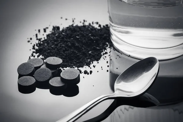 Activated carbon in tablets and crushed form and a glass of water for drinking