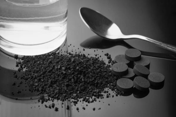 Carbono activado en granular y en tabletas con una cuchara y un vaso de agua — Foto de Stock