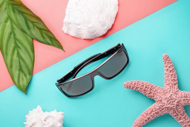Bir yaz tatili konsepti olarak renkli bir arka plan üzerinde denizyıldızı ile güneş gözlüğü ve deniz kabukları.