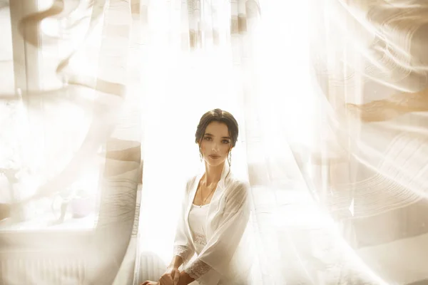 Novia en hermoso vestido sentado en la silla en el interior del estudio blanco como en casa. Estilo de boda de moda tiro . — Foto de Stock