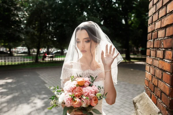 Hermosa novia con velo nupcial en la cara posando cerca de la pared roja de la antigua iglesia gótica — Foto de Stock