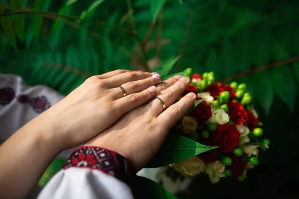 Los detalles de boda - el primer plano de las manos de los recién casados con los anillos de oro sobre el fondo verde —  Fotos de Stock