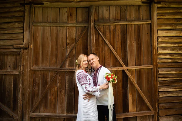 Matrimonio etnico in costumi nazionali. Sposi e sposi ucraini in stile ucraino sono in piedi con bouquet sullo sfondo di una parete di legno — Foto Stock