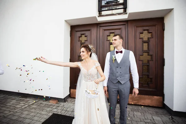 Прекрасная невеста держит корзину конфет и разбрасывает их возле церкви — стоковое фото