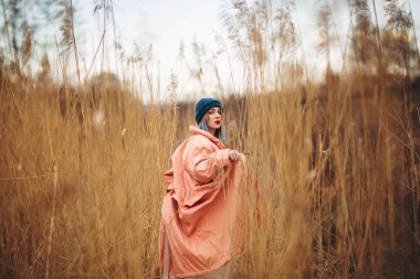 Pastel kat giyen genç bir kız ve şık bir şapka bir buğday alanında pozlar. Geri viev