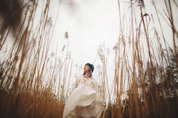 Una joven con un elegante sombrero y vestido blanco caminando en un campo de trigo — Foto de Stock