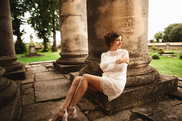 Mujer joven en vestido blanco sentada cerca de las viejas columnas — Foto de Stock