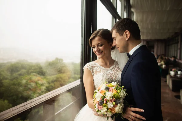 Novia y novio con un ramo de pie en la terraza con vista a la naturaleza verde —  Fotos de Stock