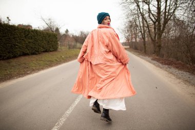 Güzel bir ceket ve beyaz elbise içinde bir kadın yol boyunca sürmek. Geri viev