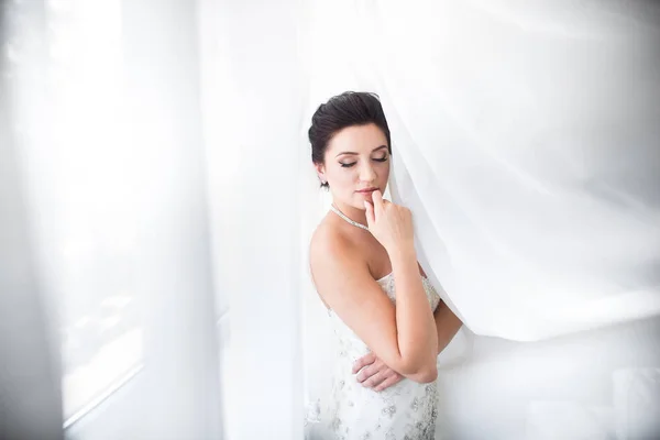 Hermosa novia sexy en vestido blanco posando bajo la cortina — Foto de Stock