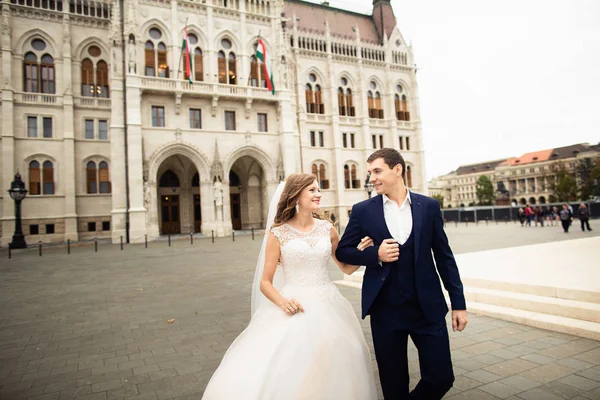 Menyasszony és vőlegény átölelve a régi város utcán. Esküvő pár séta Budapesten a Parlamentház közelében. — Stock Fotó