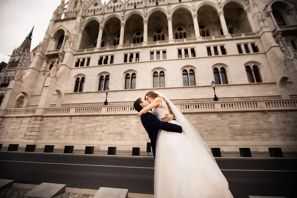 Menyasszony és vőlegény átölelve a régi város utcán. Esküvő pár séta Budapesten a Parlamentház közelében. — Stock Fotó
