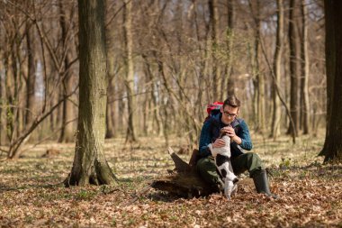 Sırt çantalı genç bir adam köpeğiyle ormanda yürüyüş yapıyor. Doğa ve fiziksel egzersiz kavramı