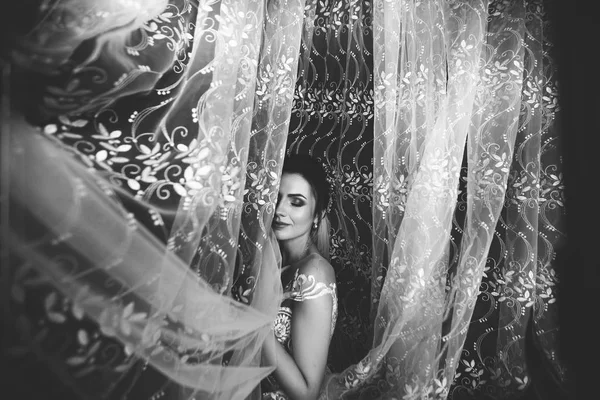 Schönen Brautstil. Hochzeitsmädchen stehen im luxuriösen Hochzeitskleid am Fenster. schwarz-weiß — Stockfoto