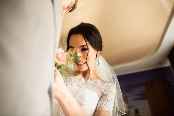 Traditionnellement, la mariée dans la maison touche un petit bouquet pour le marié. Bouquet de chambre à côté de la main sur le costume — Photo