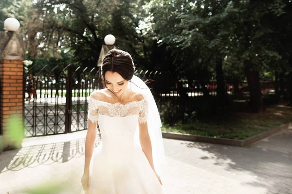 Hermosa joven novia en vestido blanco con estilo, sonriendo se encuentra con su novio en el parque — Foto de Stock