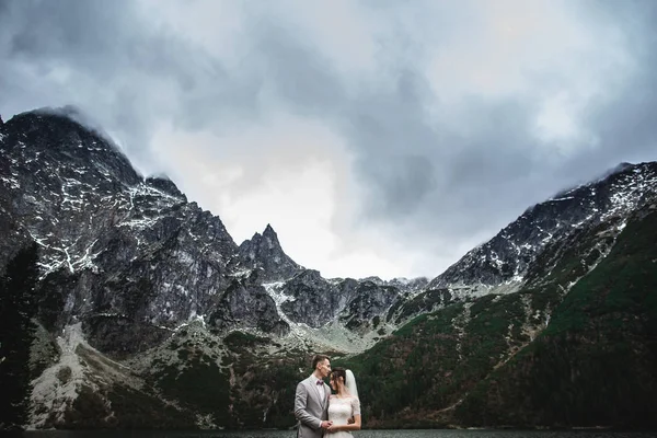 Jonge bruidspaar poserend aan de oever van het Morskie Oko meer. Polen, Tatra — Stockfoto