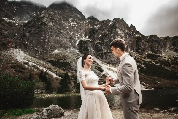 Bruidspaar wandelen en handen vasthouden aan de oever van het meer. Zonnige dag in het Tatra-gebergte — Stockfoto