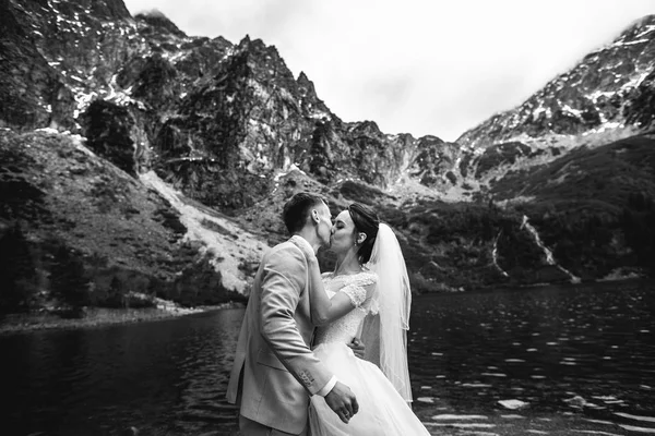 A vőlegény megcsókolta a fiatal menyasszony, a parton a tó Morskie Oko. Lengyelország. Fekete-fehér fénykép — Stock Fotó