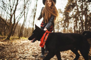Sonbahar parkında köpeği olan genç bir kız. Kızın güzel siyah bir şapkası var..