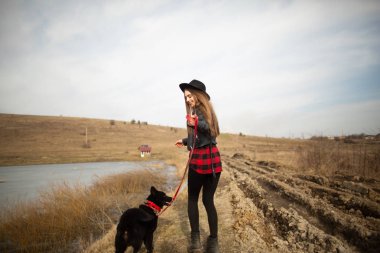 Genç bir kız bir gölün kıyısında bir köpekle yürüyor. Geri görünüm