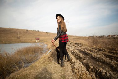 Genç bir kız bir gölün kıyısında bir köpekle yürüyor. Geri görünüm