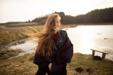 Bir genç kız bir göl kıyısında pozlar, ona bir eşarp atma