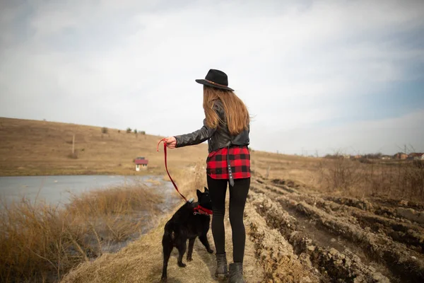 Genç bir kız bir gölün kıyısında bir köpekle yürüyor. Geri görünüm