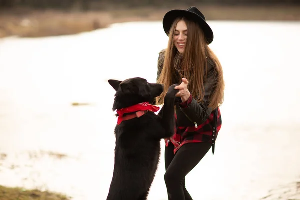 Giovane donna in cappello nero divertirsi con il suo cane. Immagine scattata in campagna — Foto Stock
