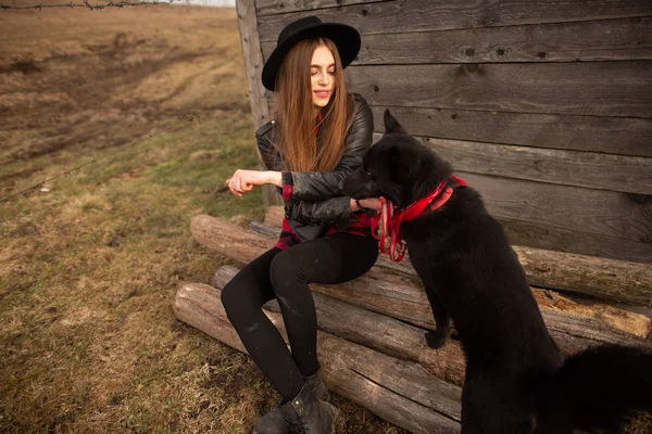 古い木造家屋のフロンの黒犬と座っている幸せな若い女 — ストック写真