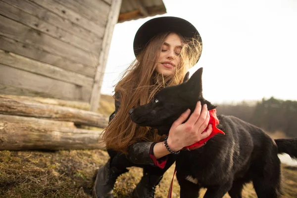 Glückliche junge Frau mit ihrem schwarzen Hund brovko vivchar vor einem alten Holzhaus. — Stockfoto