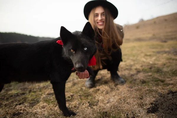Glückliche junge Frau mit schwarzem Hut, die mit ihrem schwarzen Hund am Ufer des Sees steht — Stockfoto