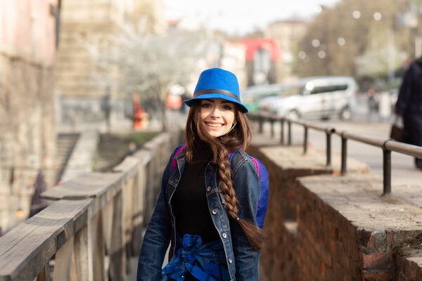 Молодая стильная женщина идет по старой улице города, путешествует с рюкзаком и синей шляпой. Украина, Львов
