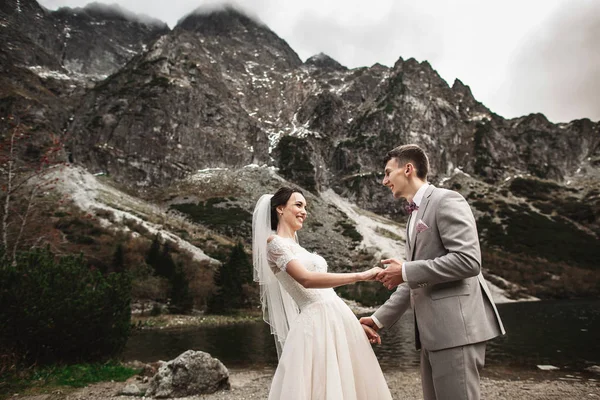 웨딩 부부는 호숫가에서 걷고 손을 잡고 있습니다. 타트라 산맥의 화창한 날 — 스톡 사진