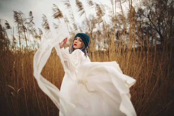 Ein junges Mädchen mit stylischem Hut und weißem Kleid, das in einem Weizenfeld spaziert — Stockfoto