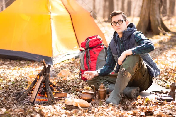 A young traveler in the forest is resting near the tent and cook