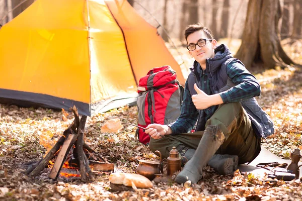A young traveler in the forest is resting near the tent and cook